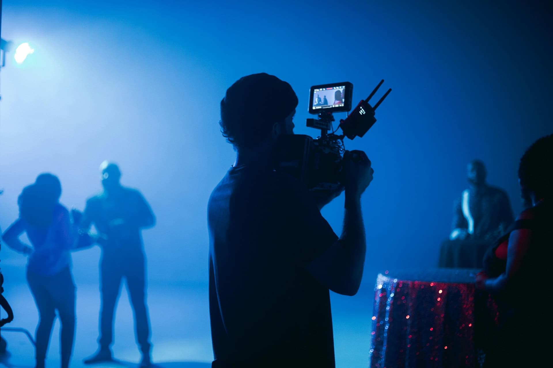 A cameraperson filming a scene with silhouettes of people in blue-tinged haze.