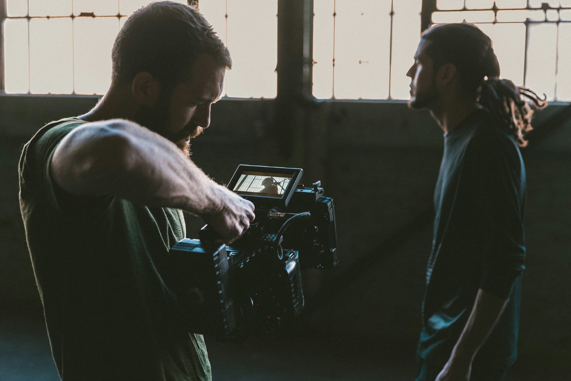 A person operating a camera with another person standing in profile.