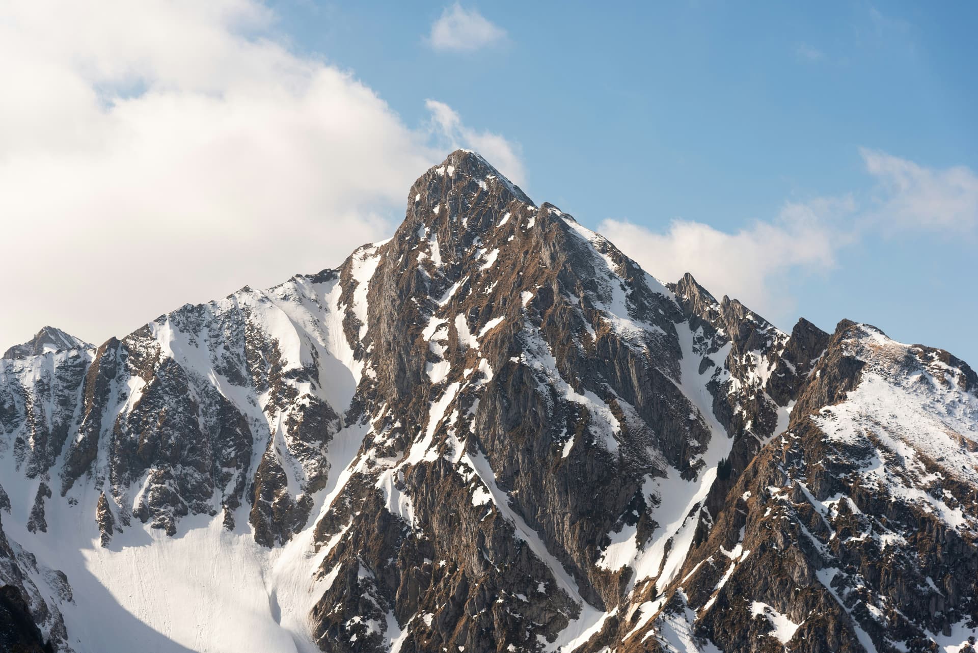 Snow-capped rugged mountain peak under a blue sky with clouds.