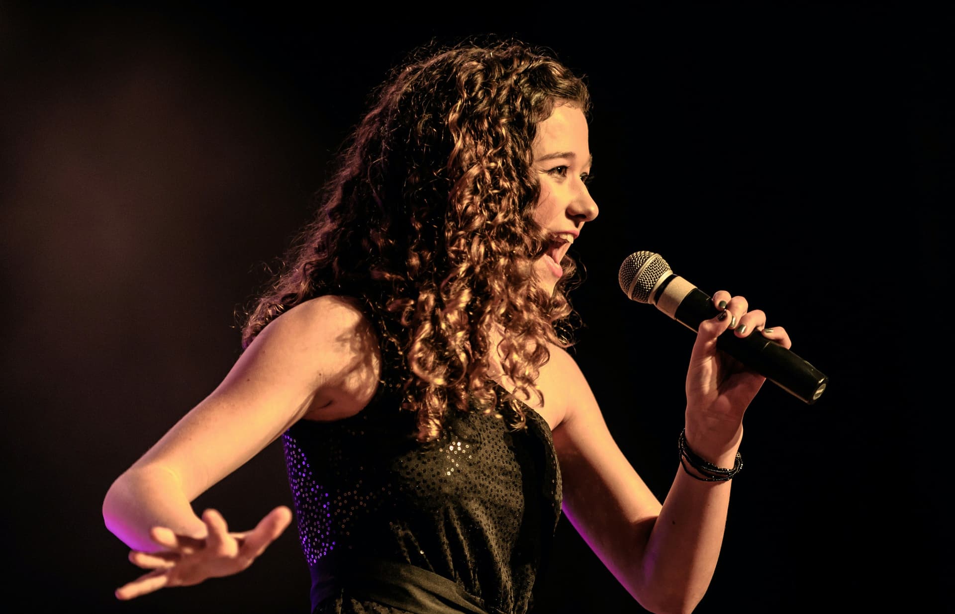 A curly-haired singer holding a microphone on stage.